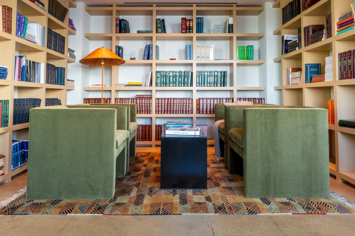 A well lit library with four green chairs facing each other.