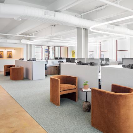 A well lit office space featuring shared desks and brown accent chairs