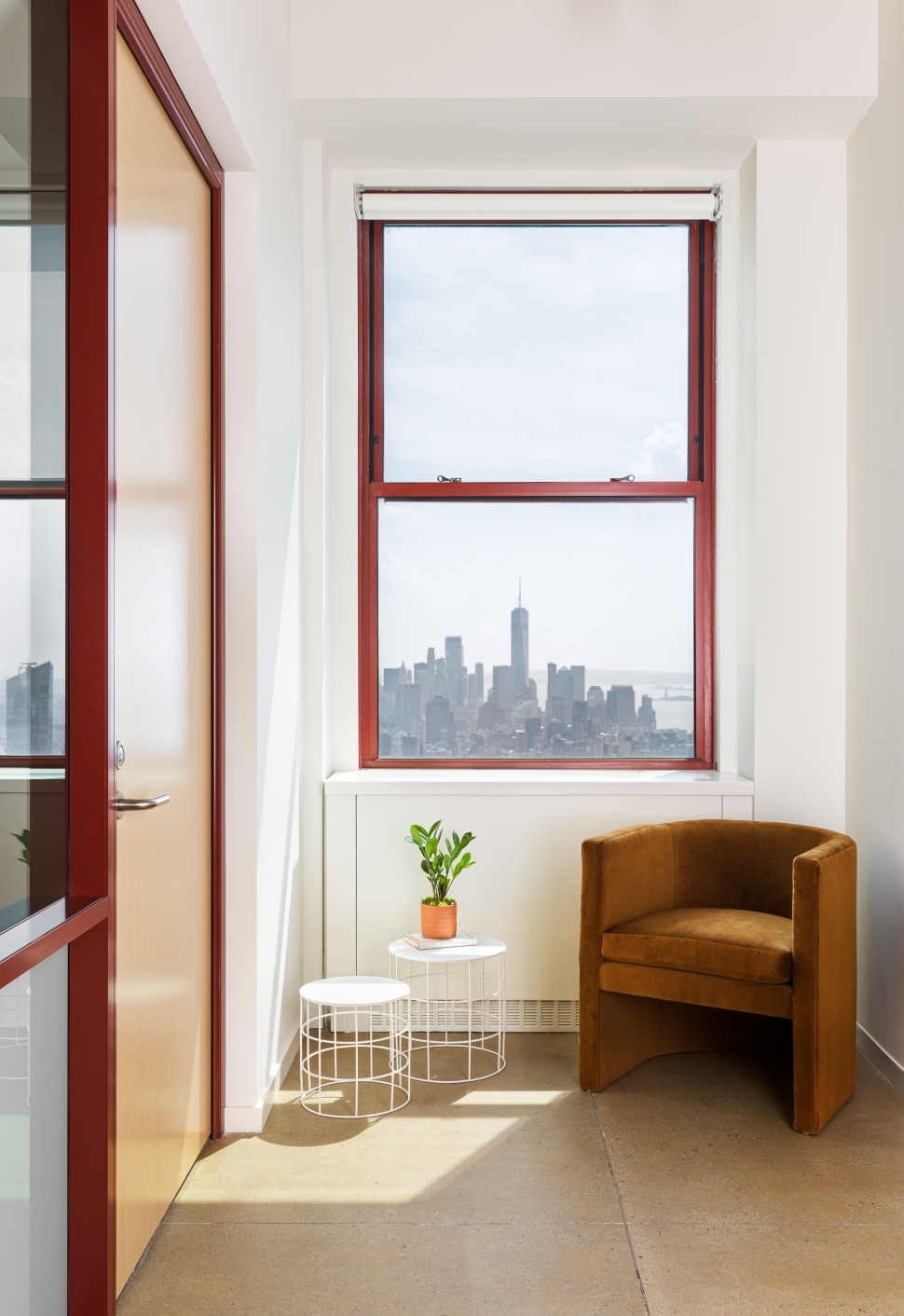 A brown accent chair sits in front of a window featuring a bright city skyline.