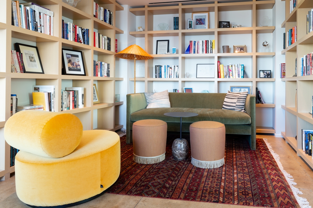 A well lit library featuring a green couch and yellow, circular accent chair